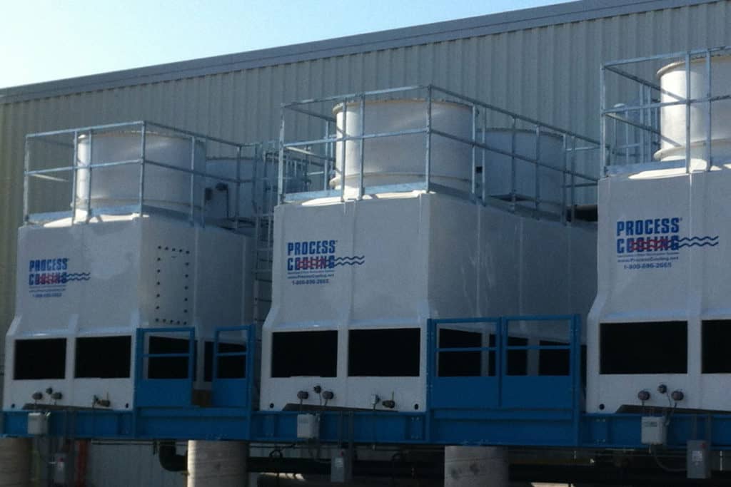 An outdoor view of Process Cooling's cooling towers in the shade against a white building.